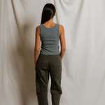 Person wearing a gray tank top and green pants standing against a plain white background