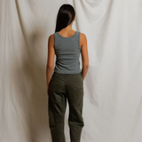 Person wearing a gray tank top and green pants standing against a plain white background