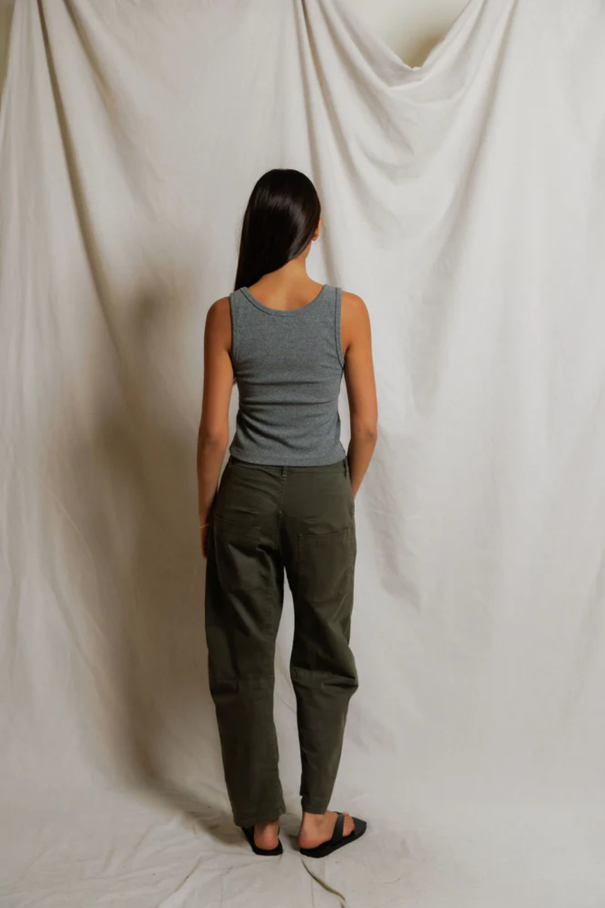 Person wearing a gray tank top and green pants standing against a plain white background