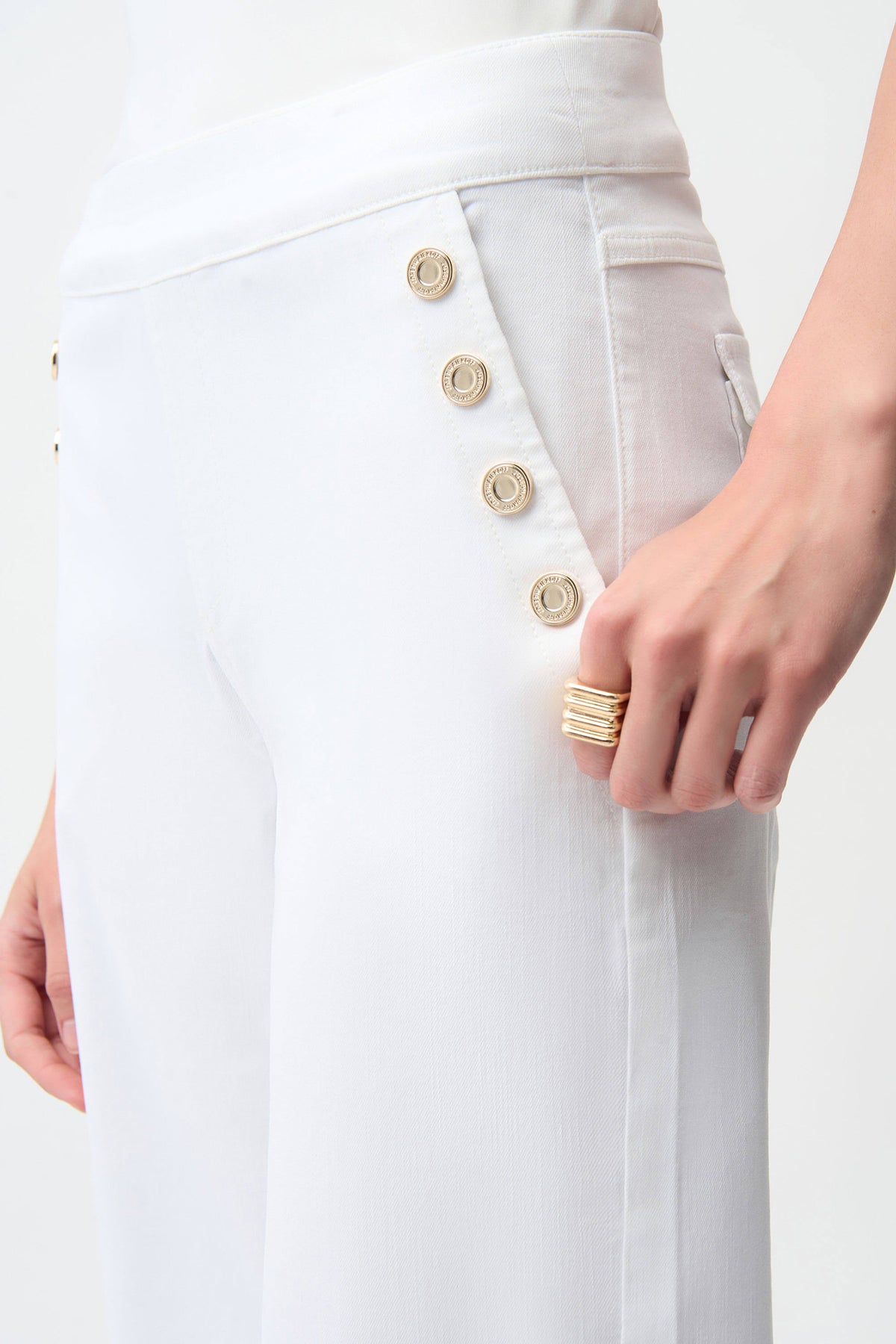 Close-up of a white coat with gold buttons and a hand wearing a ring on a white background