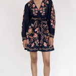 A woman modeling a navy blue long-sleeve mini dress with a pink and green floral print, standing against a plain white studio background.