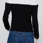 A person shown from the back wearing a color-block knit sweater with a white yoke and black sleeves, paired with blue jeans, against a light gray studio background.