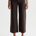 A model wearing dark brown cropped wide-leg jeans with a raw hem, styled with a white top and black loafers against a plain white studio background.