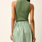 Woman wearing a green sleeveless top and green and white striped pants on a beige background