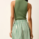 Woman wearing a green sleeveless top and green and white striped pants on a beige background
