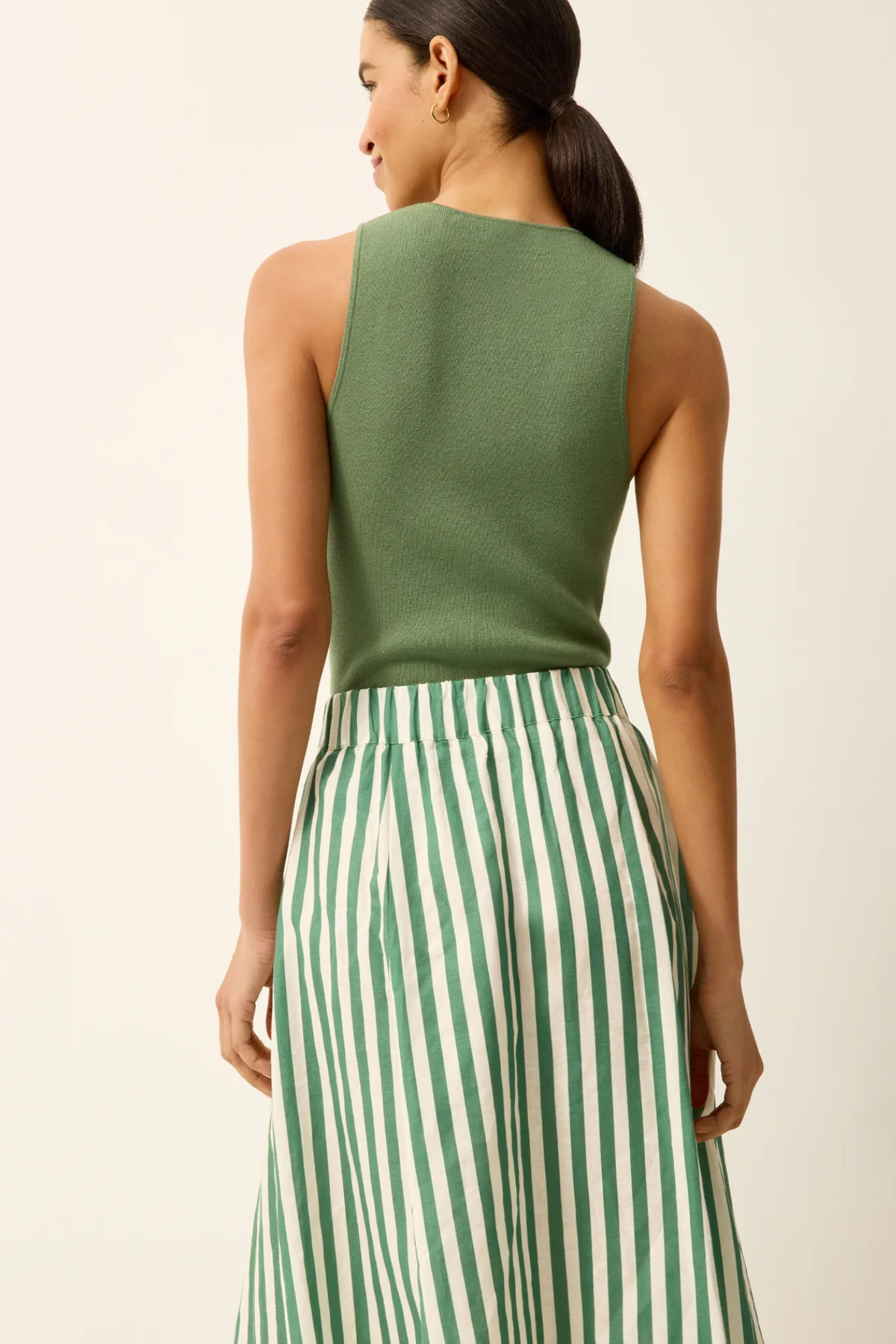 Woman wearing a green sleeveless top and green and white striped pants on a beige background