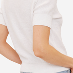 Close-up back view of a person wearing a short-sleeve white knit top with light blue jeans against a plain light background.