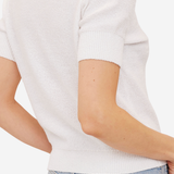 Close-up back view of a person wearing a short-sleeve white knit top with light blue jeans against a plain light background.