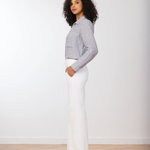 Woman wearing a gray sweater and white pants standing against a plain white background