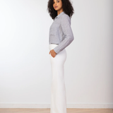Woman wearing a gray sweater and white pants standing against a plain white background