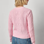 Person wearing a pink knitted sweater and blue jeans on a plain background