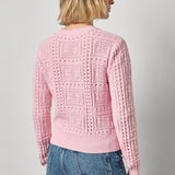 Person wearing a pink knitted sweater and blue jeans on a plain background