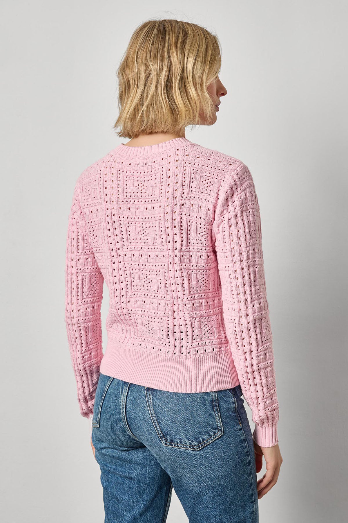 Person wearing a pink knitted sweater and blue jeans on a plain background