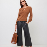 A woman modeling a brown long-sleeve knit top with a crossover front and keyhole cutout, paired with black wide-leg pants, leopard-print heeled mules, sunglasses, and a brown textured tote bag against a plain light gray studio background.