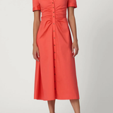 Woman wearing a coral dress with buttons on a white background