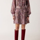 Person wearing a patterned dress with a belt and red knee-high boots on a white background