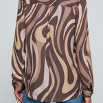 Model wearing a long-sleeve abstract print blouse in warm neutral tones paired with blue denim.