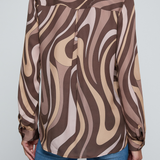 Model wearing a long-sleeve abstract print blouse in warm neutral tones paired with blue denim.