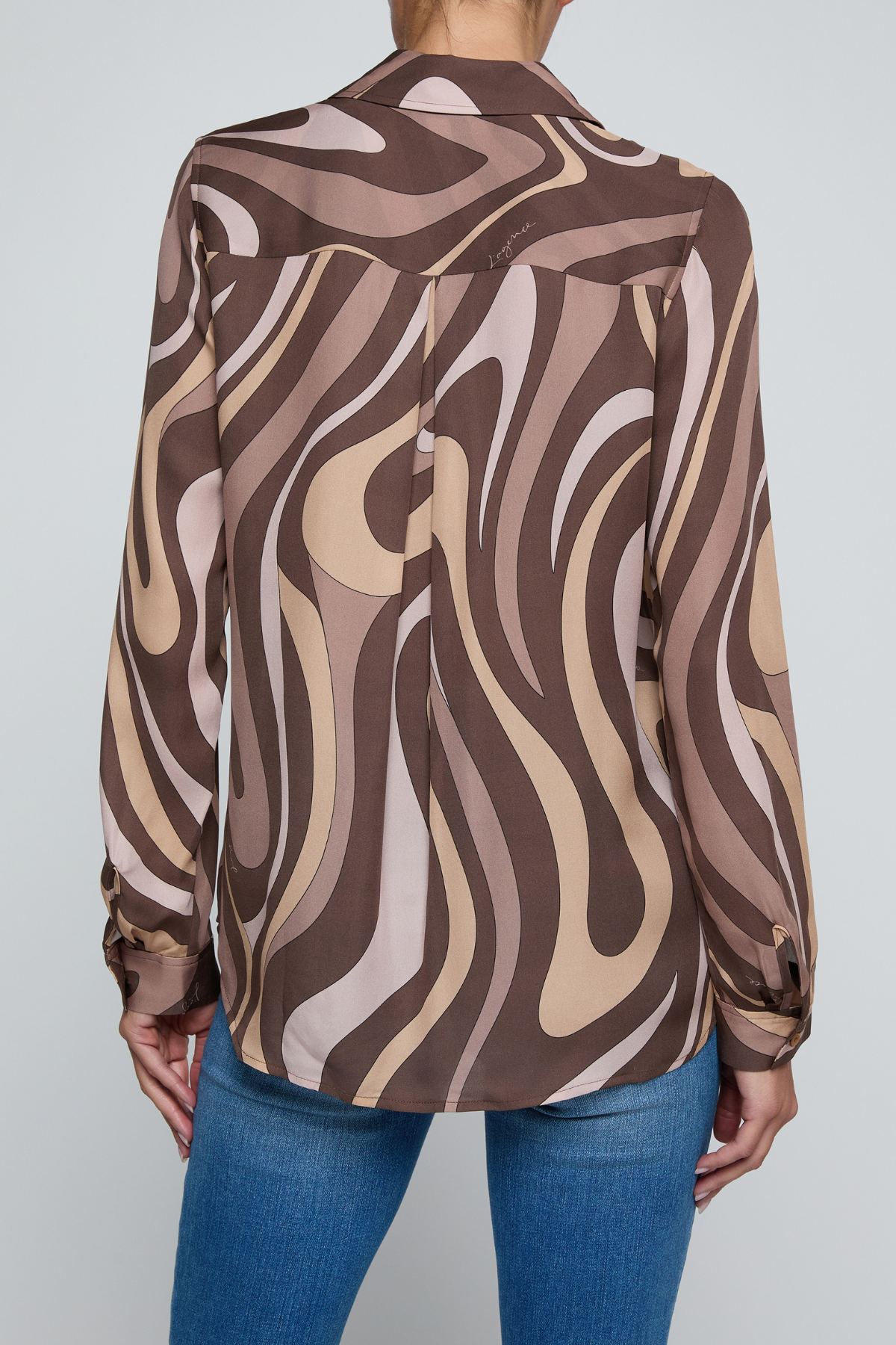 Model wearing a long-sleeve abstract print blouse in warm neutral tones paired with blue denim.