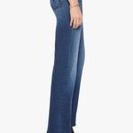A side profile view of a model wearing blue high-waisted flare jeans, paired with a white top and black pointed-toe ankle boots, against a plain white background.