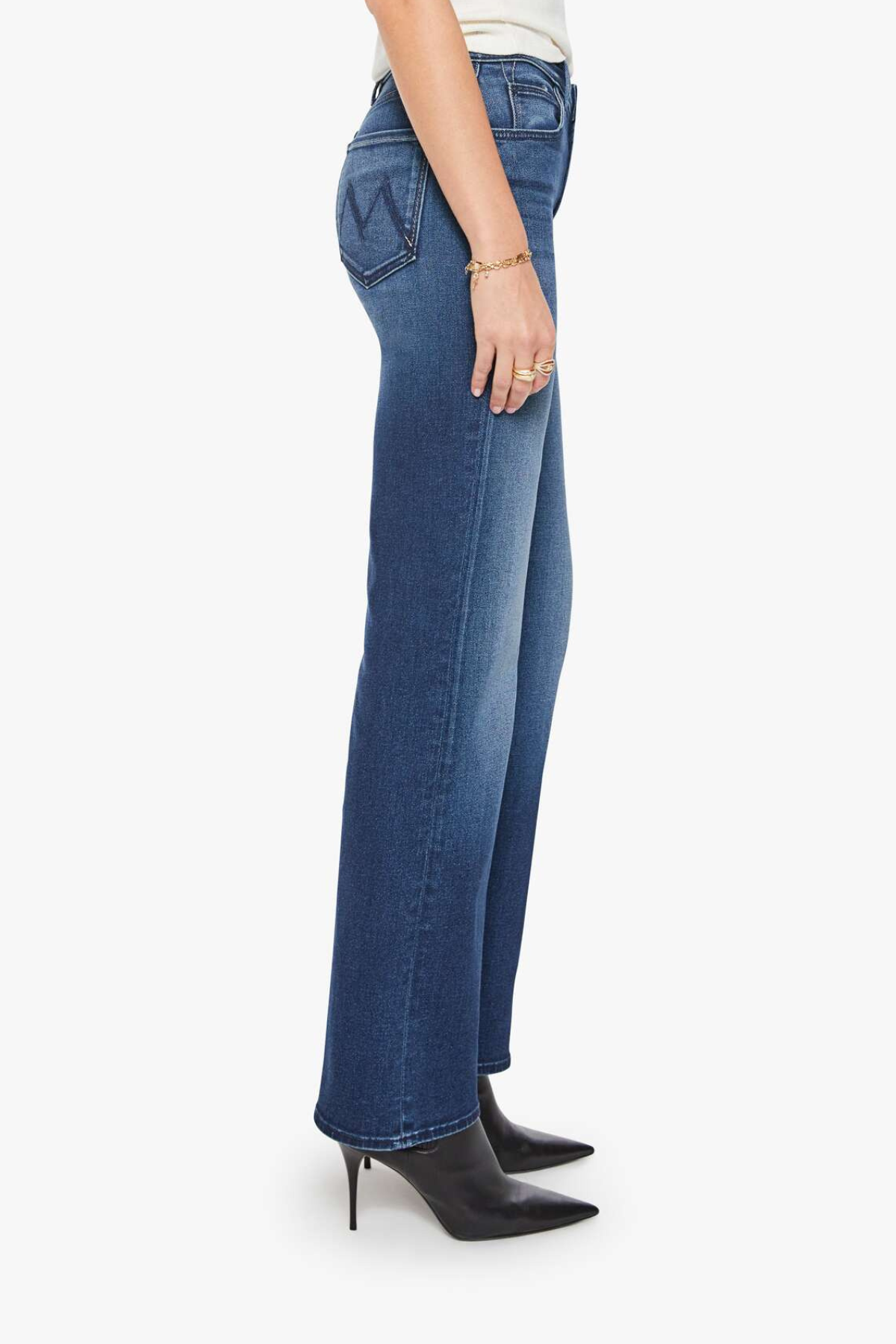 A side profile view of a model wearing blue high-waisted flare jeans, paired with a white top and black pointed-toe ankle boots, against a plain white background.