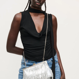 Woman holding a silver fringed handbag against a plain background