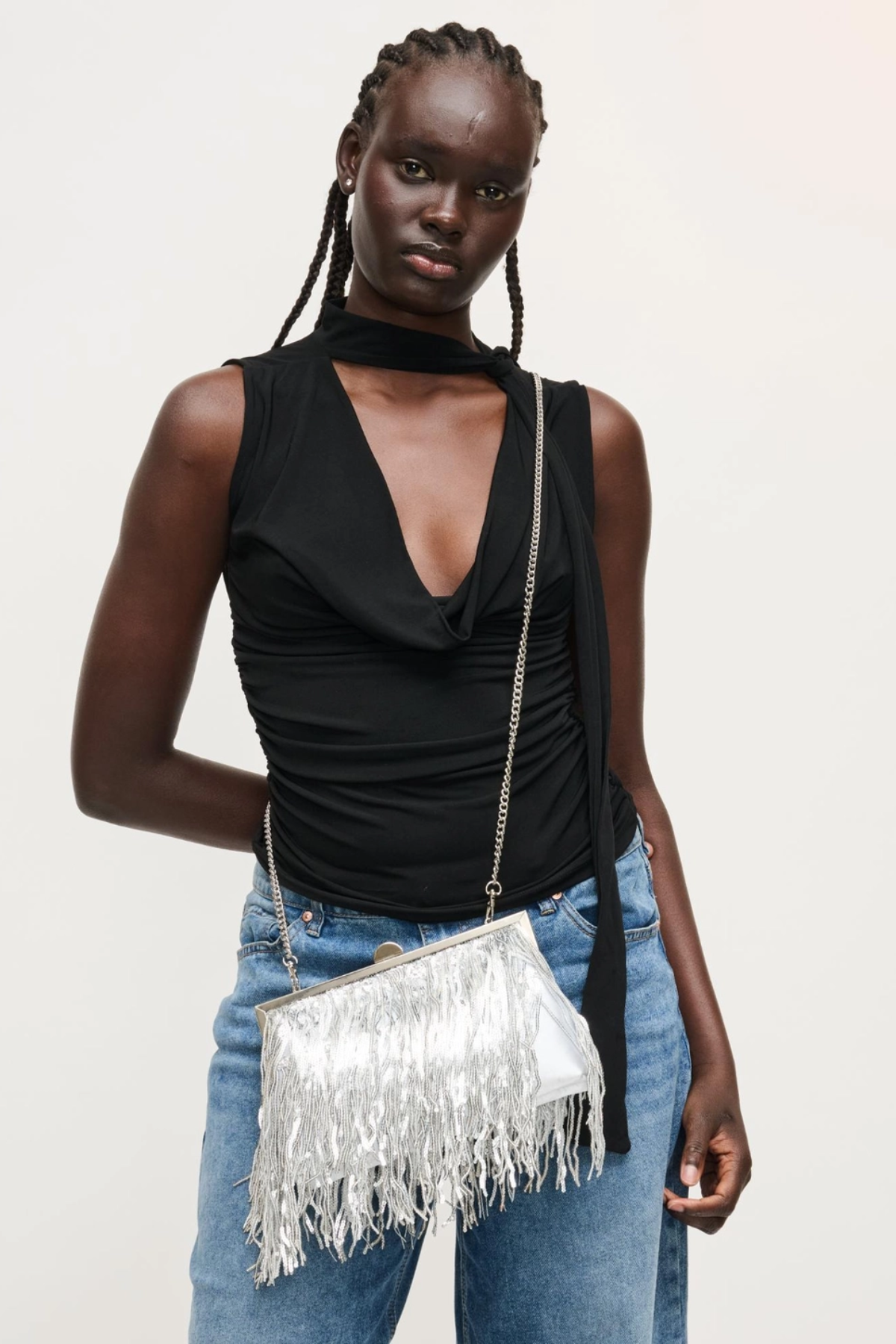Woman holding a silver fringed handbag against a plain background