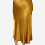 A model wearing a satin midi skirt in a rich mustard yellow color, paired with beige high-heeled sandals, shown from the waist down against a plain white background.
