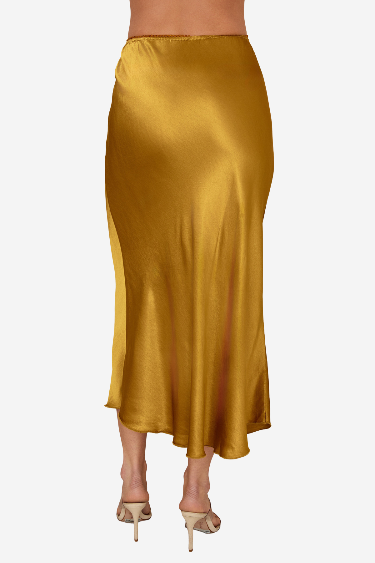A model wearing a satin midi skirt in a rich mustard yellow color, paired with beige high-heeled sandals, shown from the waist down against a plain white background.