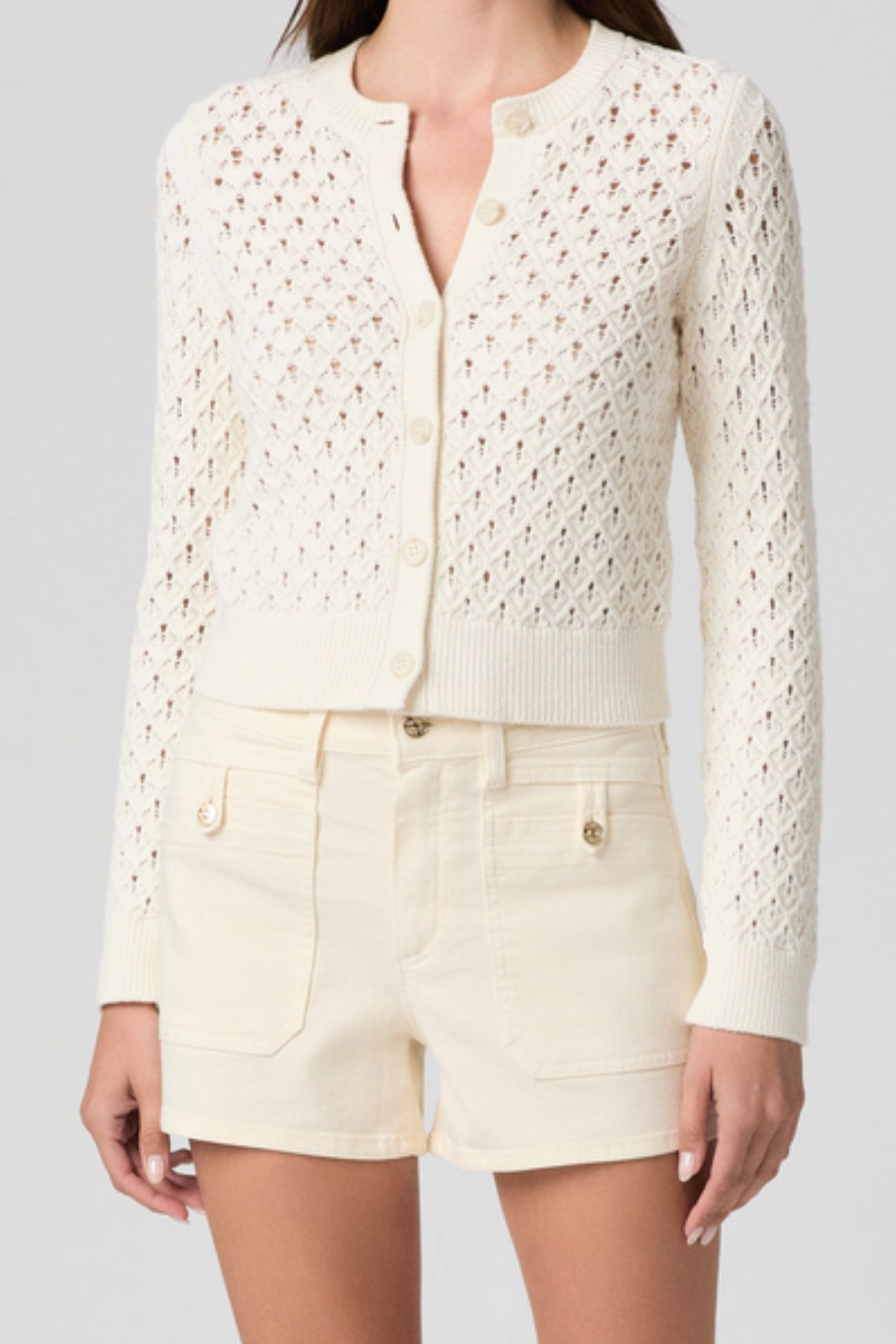 Person wearing a white lace cardigan and shorts on a gray background