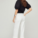 Woman wearing a black top and white pants on a plain background