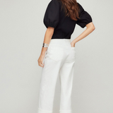 Woman wearing a black top and white pants on a plain background