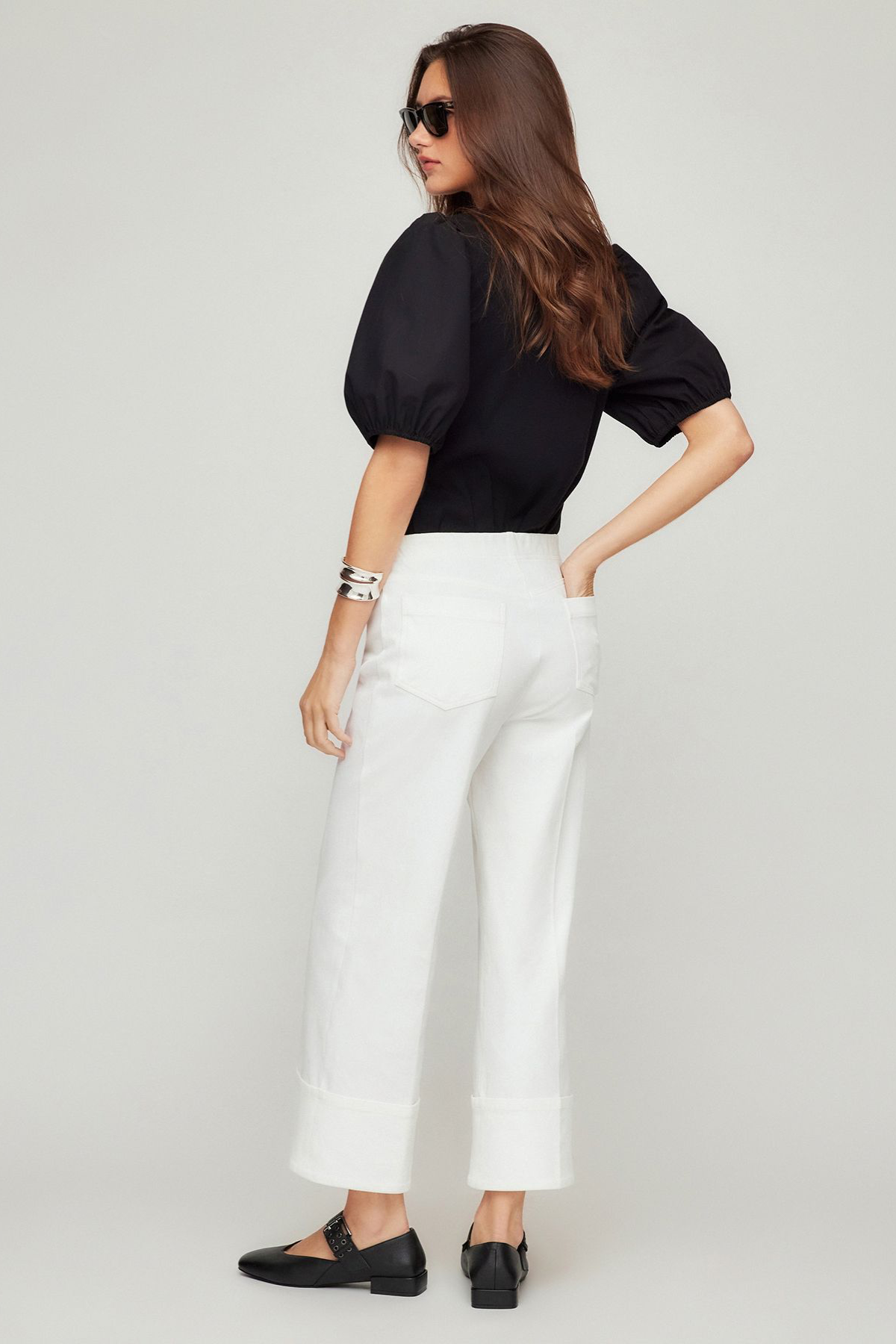 Woman wearing a black top and white pants on a plain background