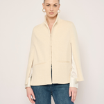 A woman modeling a cream-colored jacket with satin sleeves and blue jeans, standing against a plain light background.
