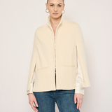A woman modeling a cream-colored jacket with satin sleeves and blue jeans, standing against a plain light background.