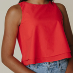 Person wearing a red sleeveless top and blue jeans against a neutral background