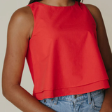 Person wearing a red sleeveless top and blue jeans against a neutral background