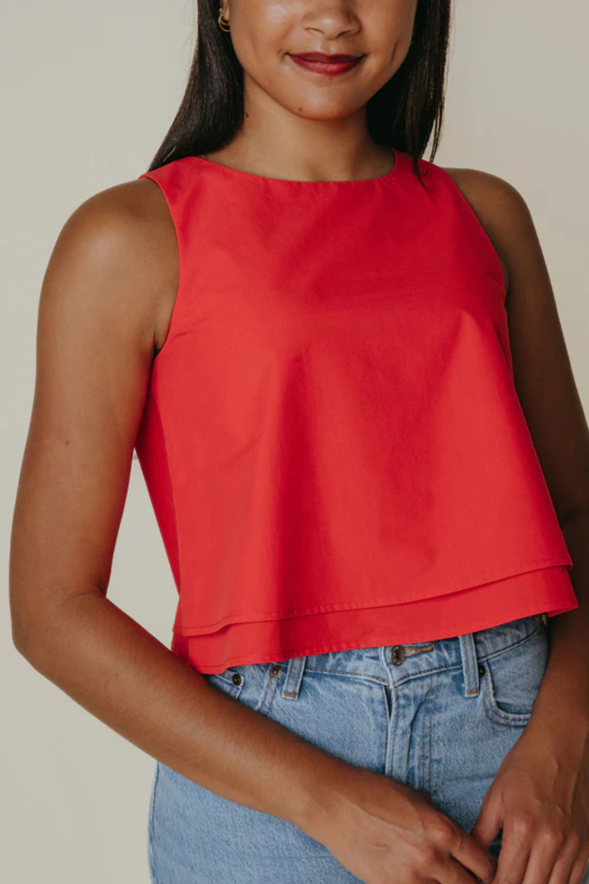 Person wearing a red sleeveless top and blue jeans against a neutral background