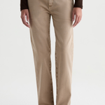 A person wearing straight-leg beige jeans with a dark brown long-sleeve top and dark brown woven loafers, shown from the waist down against a light gray studio background.