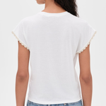 A woman shown from the back wearing a white short-sleeve t-shirt with delicate scalloped edges on the sleeves, paired with light blue jeans, against a plain white background.