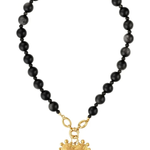 A beaded necklace featuring matte black round beads and a textured gold heart-shaped pendant, displayed on a clean white background.