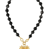 A beaded necklace featuring matte black round beads and a textured gold heart-shaped pendant, displayed on a clean white background.