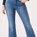 A person wearing medium-wash blue flare jeans with a black belt and gold buckle, paired with a black blouse, shown from the waist down against a plain light background.