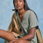 Woman wearing a green outfit with a beige jacket against a blue textured background