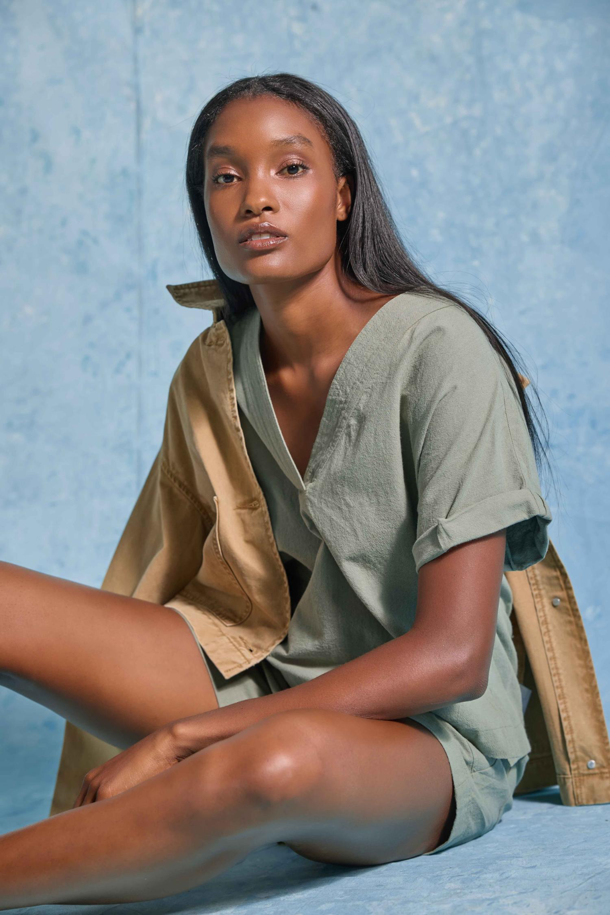 Woman wearing a green outfit with a beige jacket against a blue textured background
