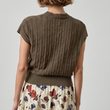 Woman wearing a brown knitted sleeveless sweater over a floral dress on a plain background