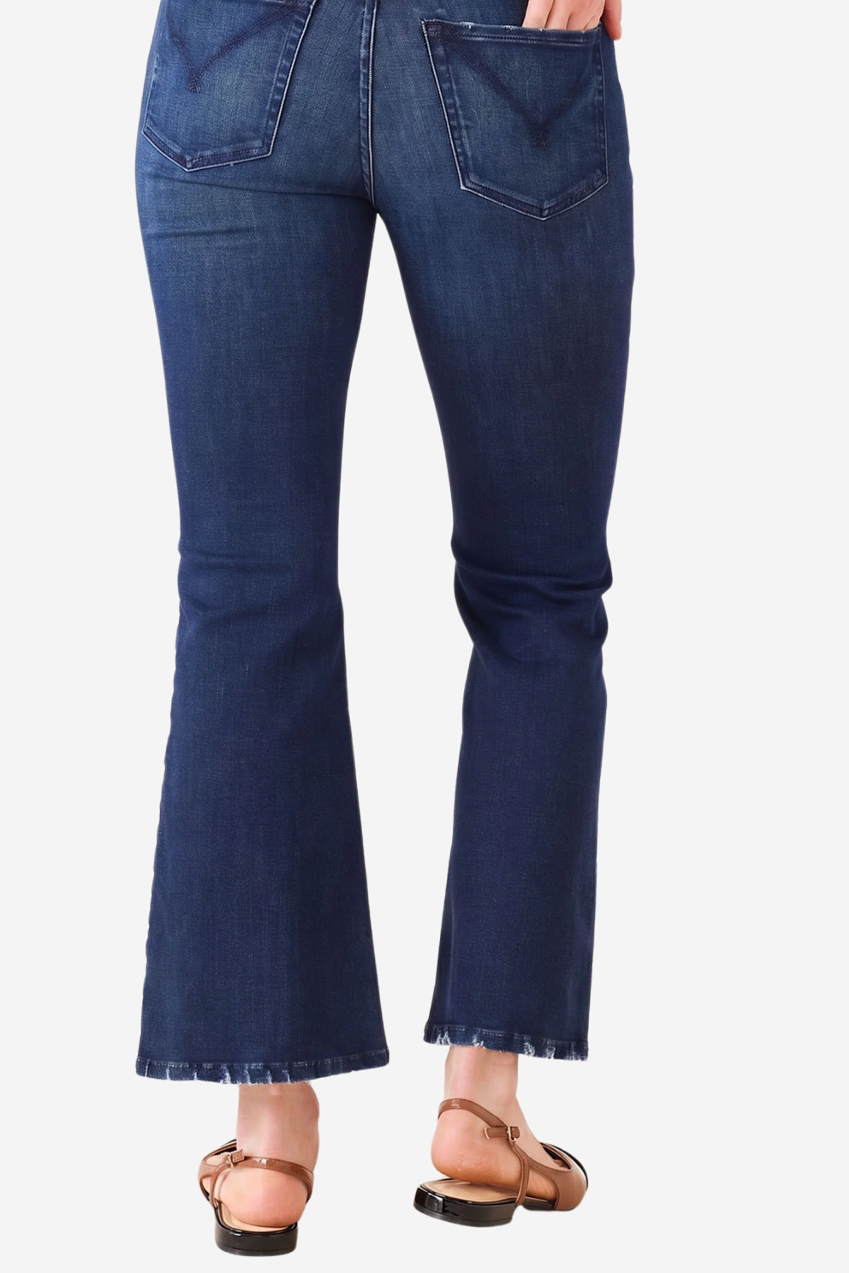 A person wearing dark blue flare jeans with frayed hems and tan flat sandals, shown from the back against a light gray background.