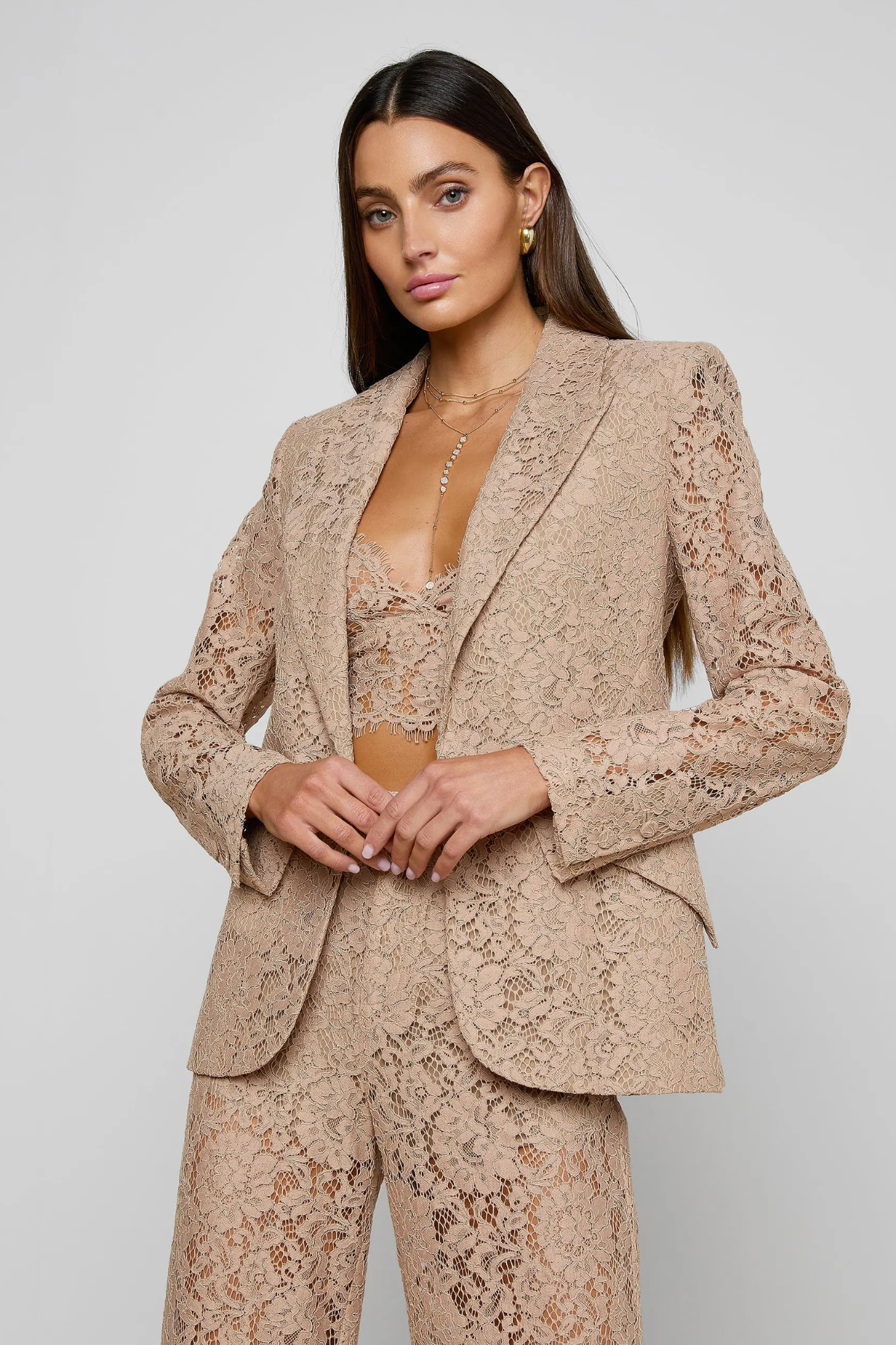 Woman wearing a beige lace suit against a plain background
