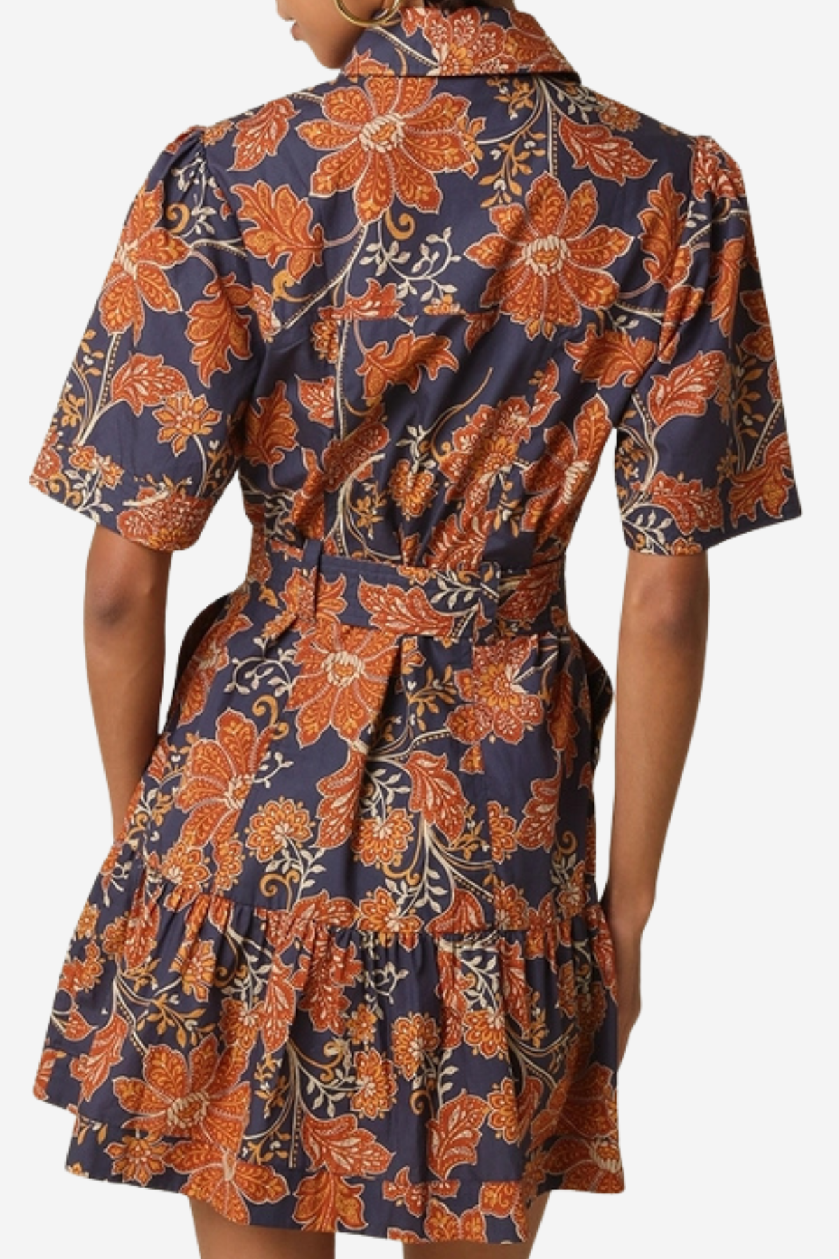 A woman wearing a short-sleeve collared dress with a tiered ruffled skirt, featuring a navy blue and rust-orange floral pattern. The photo is taken from the back against a plain light gray background.