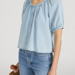 Woman wearing a light blue denim top and jeans against a plain background